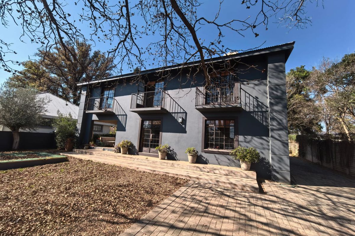Rear elevation of a two-story house featuring dark grey exterior walls, multiple balconies with metal railings, and a paved patio area.