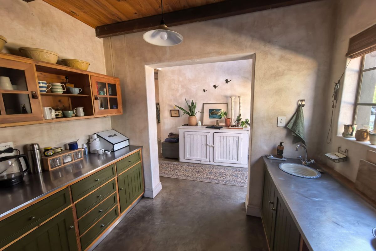 A rustic-style kitchen featuring polished concrete floors, stainless steel countertops, timber cabinetry, and an exposed timber beam ceiling.