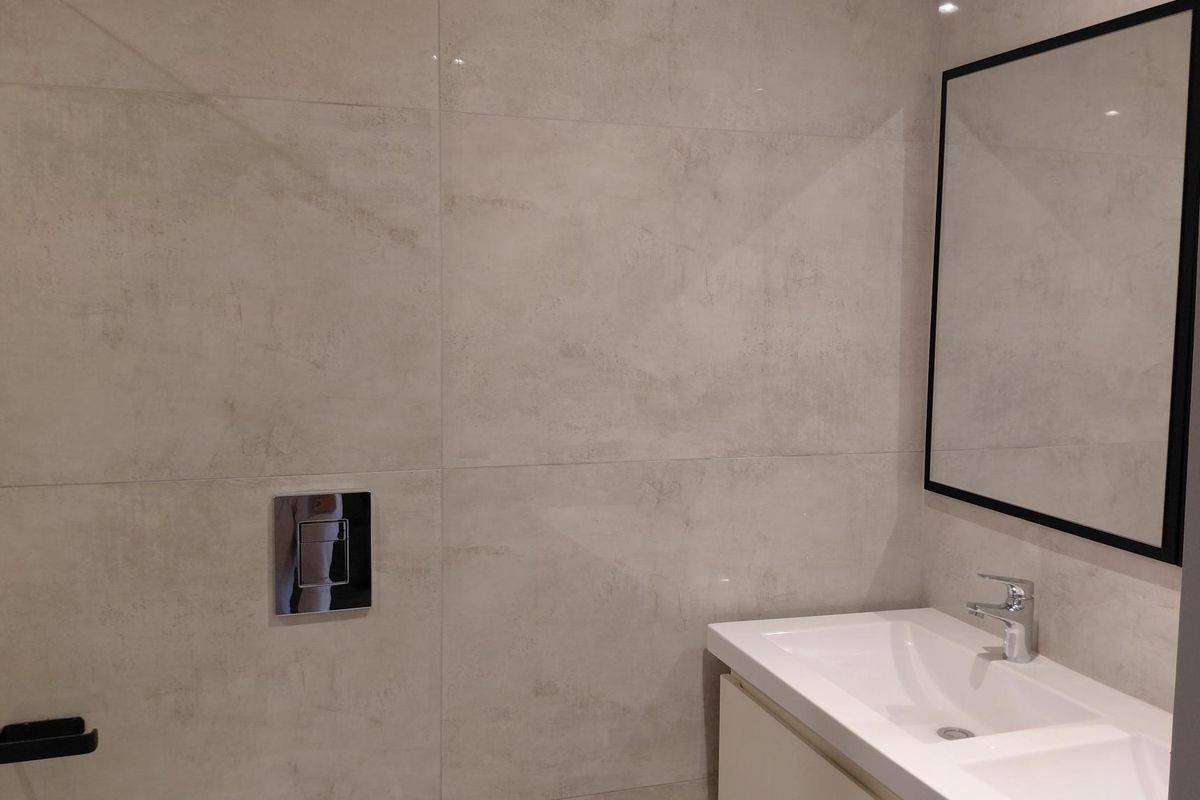 Modern bathroom featuring large format wall tiles, a sleek vanity basin with chrome mixer tap, and a wall-mounted toilet flush plate.