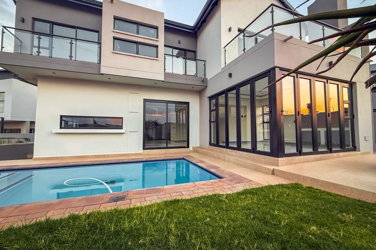 Modern double-storey residence featuring a swimming pool, expansive glass bi-fold doors, and upper-level balconies with glass balustrades.