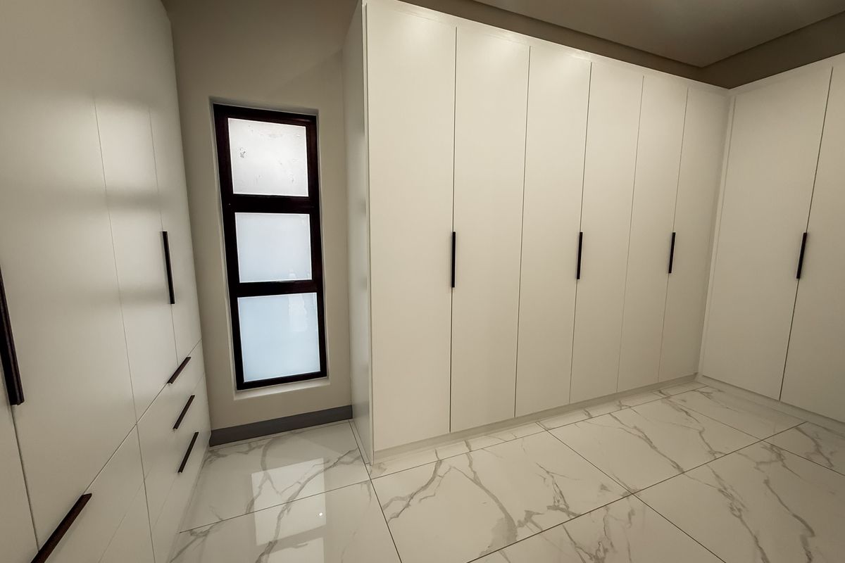 A modern, minimalist bedroom featuring extensive floor-to-ceiling built-in cabinetry, high-gloss marble-look floor tiles, and a sleek frosted glass window.