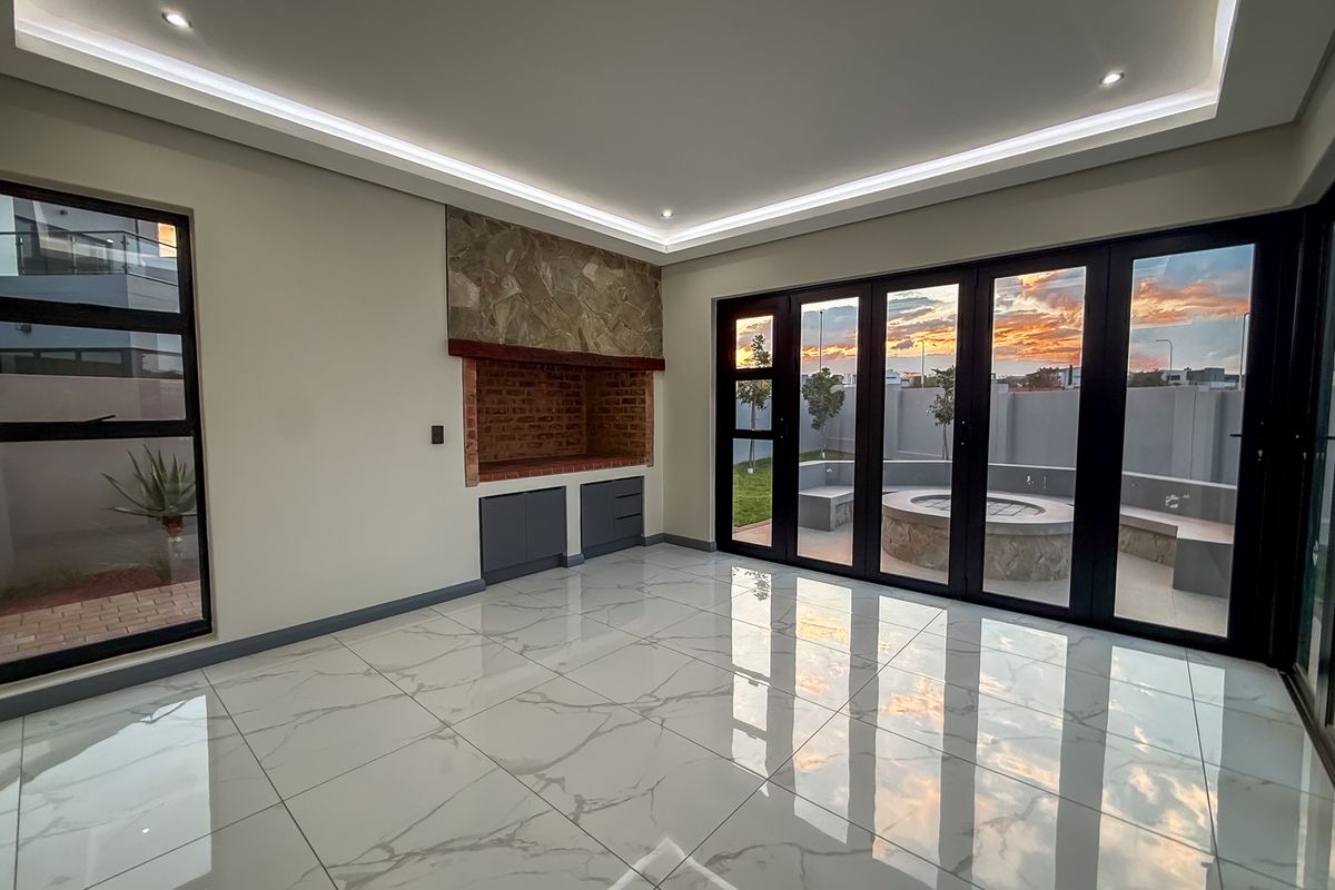 Spacious living area featuring large format porcelain tiles, recessed ceiling lighting, and a built-in braai, with seamless access to the outdoor patio through stacker doors.