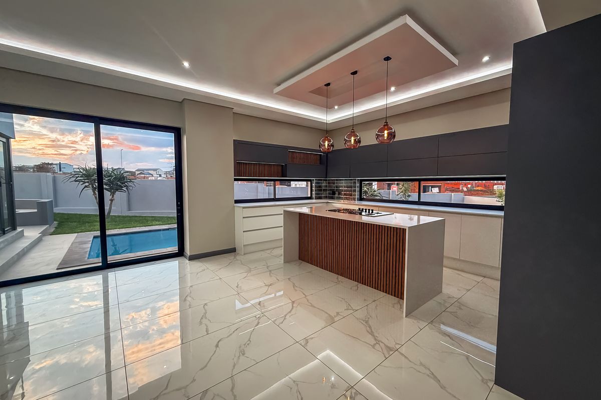 Modern, high-end kitchen featuring a central island, sleek cabinetry, stone countertops, and large sliding doors opening to a pool area with sunset views.