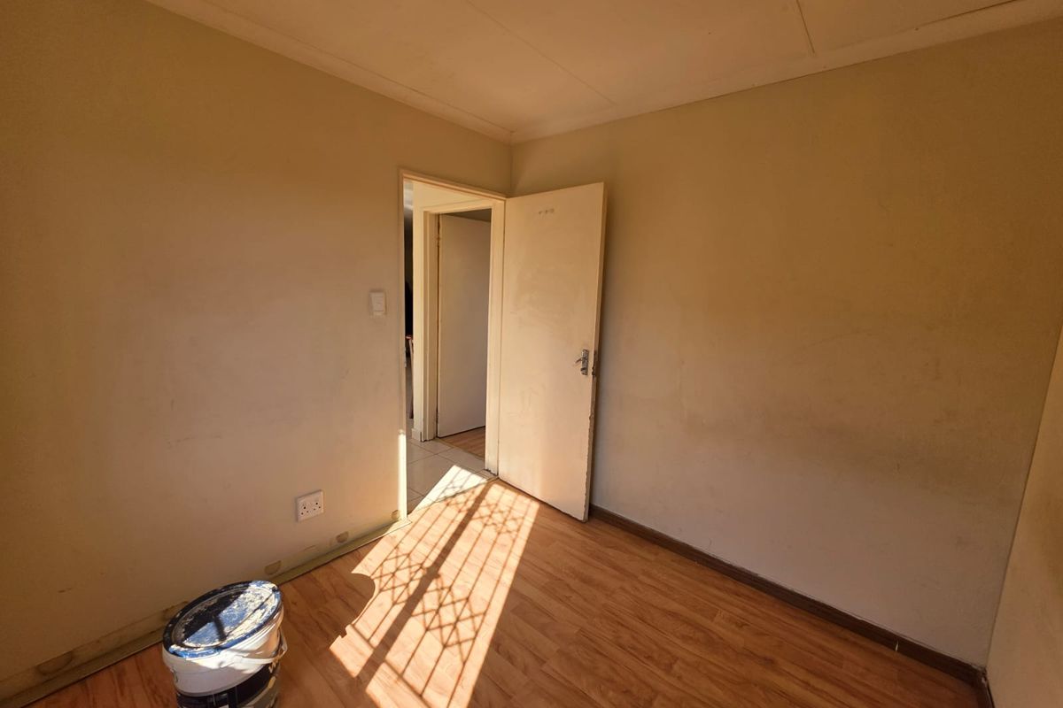 An empty bedroom featuring laminate flooring and neutral walls, currently undergoing minor maintenance or preparation for renovation.