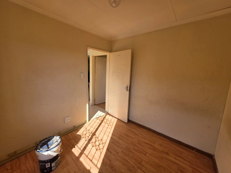 An empty bedroom featuring laminate flooring and neutral walls, currently undergoing minor maintenance or preparation for renovation.