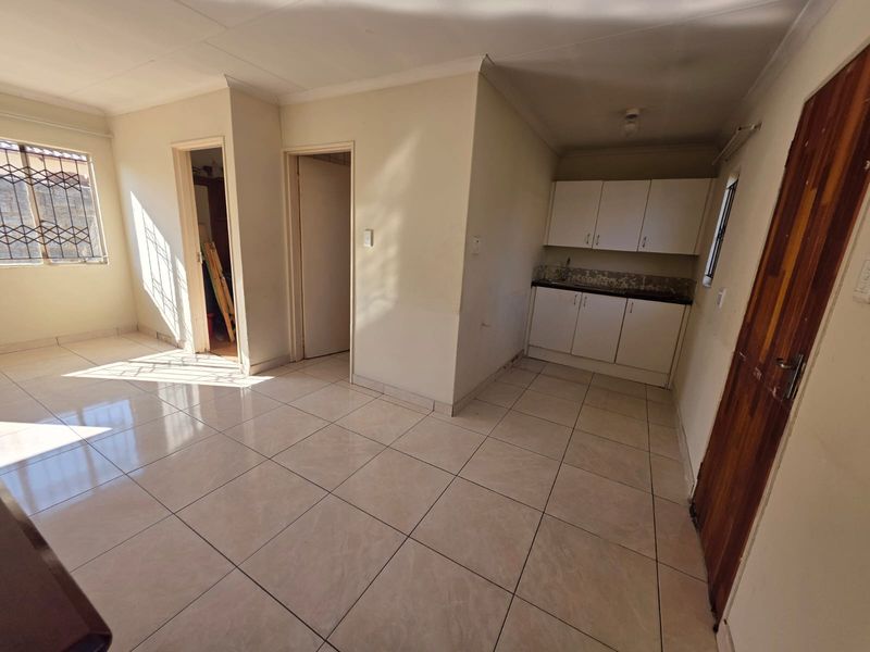 An open-plan living and kitchen area featuring tiled flooring, built-in cabinetry, and natural light, offering a blank canvas for interior design.
