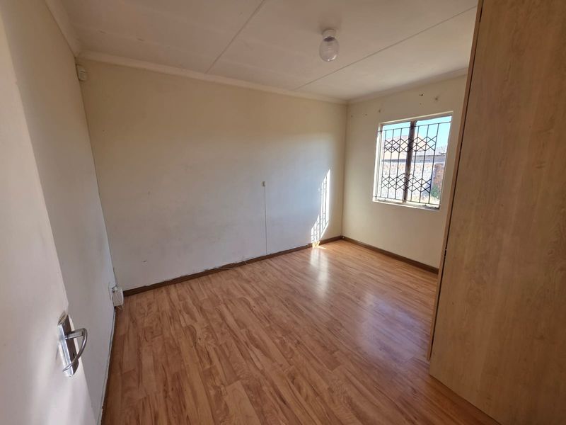 A vacant bedroom featuring laminate flooring, a built-in wardrobe, and security burglar bars on the window.