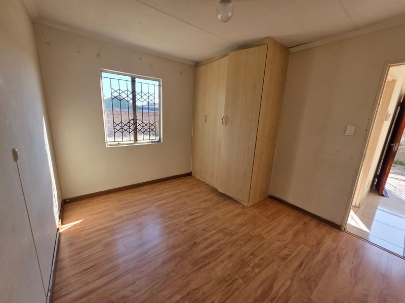 A vacant bedroom featuring laminate flooring, a built-in wardrobe, and a window fitted with a security gate.