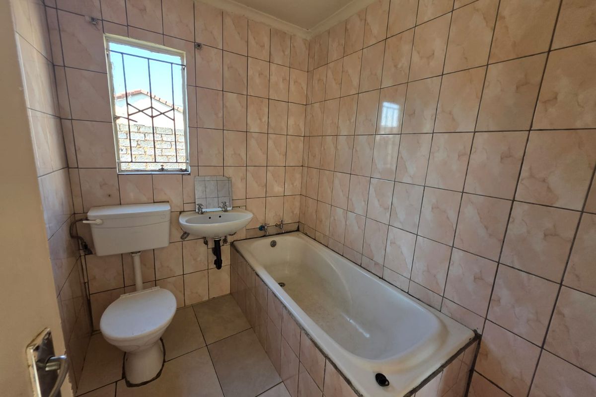 A functional bathroom featuring a bathtub, wall-mounted basin, and toilet, finished with full-height ceramic wall tiling and tiled flooring.