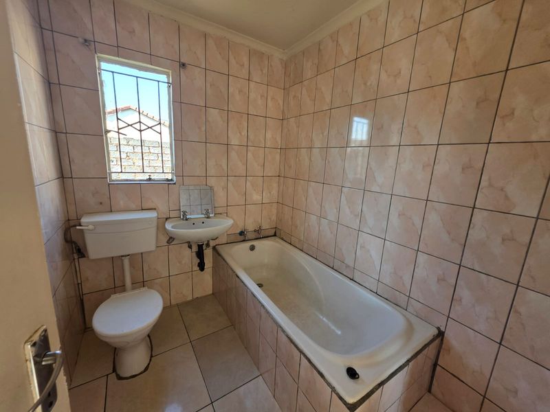 A functional bathroom featuring a bathtub, wall-mounted basin, and toilet, finished with full-height ceramic wall tiling and tiled flooring.