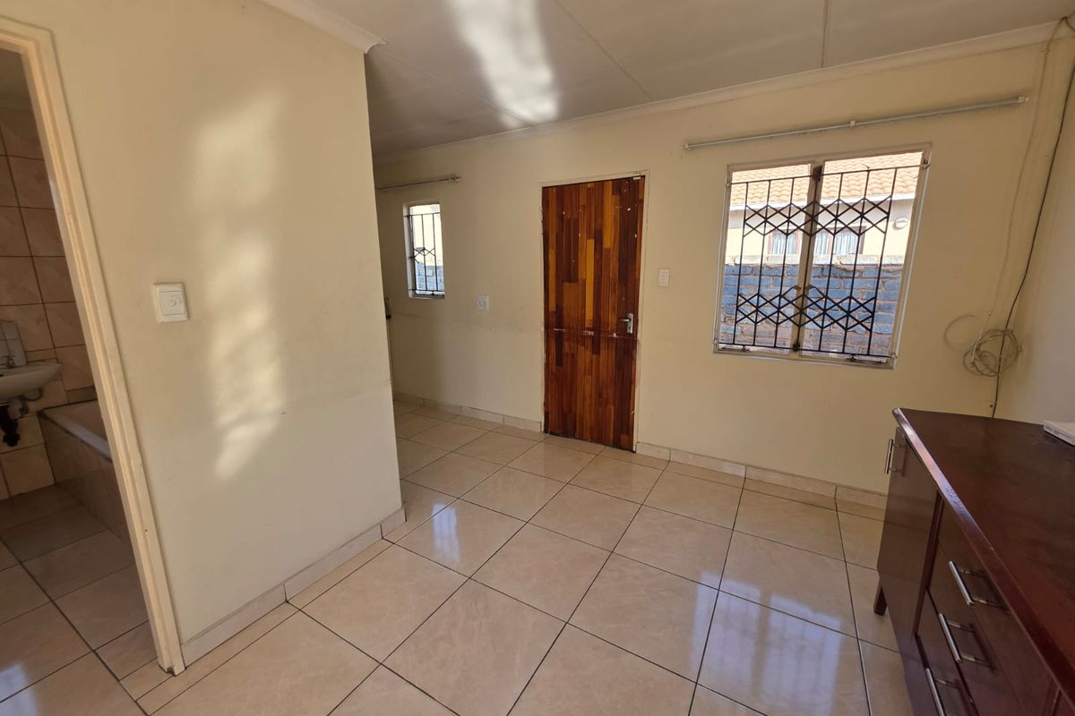 A bright, empty living area featuring tiled flooring, security gates on windows, and a wooden door, providing a neutral canvas for interior design.