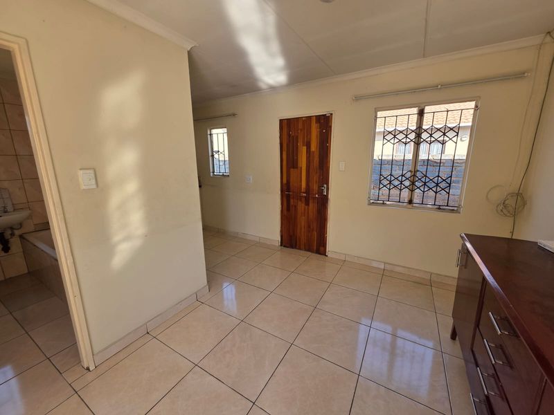 A bright, empty living area featuring tiled flooring, security gates on windows, and a wooden door, providing a neutral canvas for interior design.