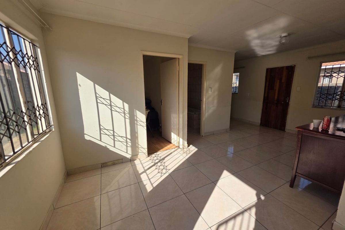 An empty living area featuring tiled flooring, security gates on windows, and neutral wall finishes, offering a blank canvas for potential interior design updates.