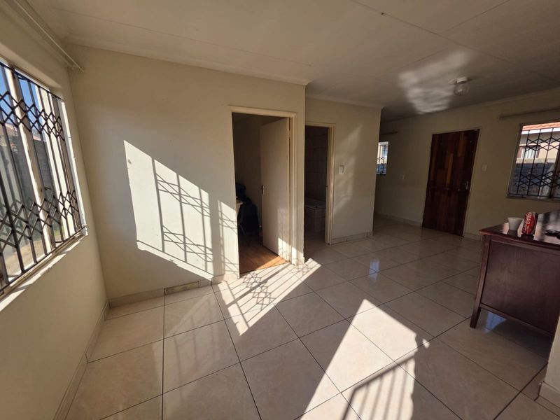 An empty living area featuring tiled flooring, security gates on windows, and neutral wall finishes, offering a blank canvas for potential interior design updates.