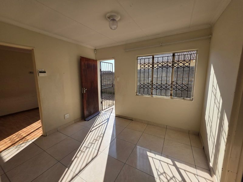 An empty living room featuring tiled flooring, security bars on windows, and a security gate leading to the exterior.