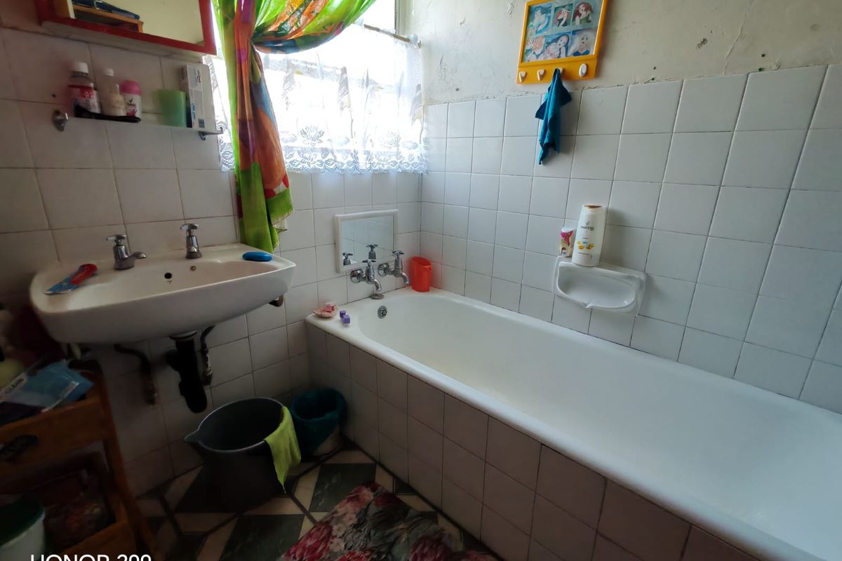 A dated bathroom featuring a built-in bathtub and wall-mounted basin, requiring cosmetic updates and wall repairs to modernize the space.