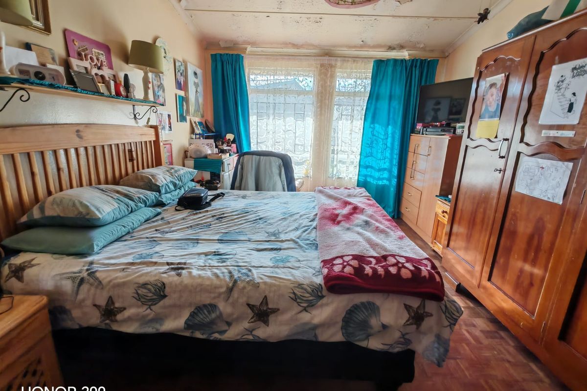 A bedroom featuring parquet flooring and security bars on the windows, currently showing significant signs of ceiling deterioration and water damage.