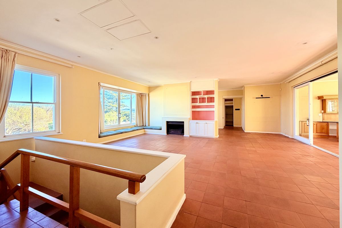 Spacious open-plan living area featuring terracotta flooring, a built-in fireplace, custom cabinetry, and large windows with integrated seating overlooking the exterior.