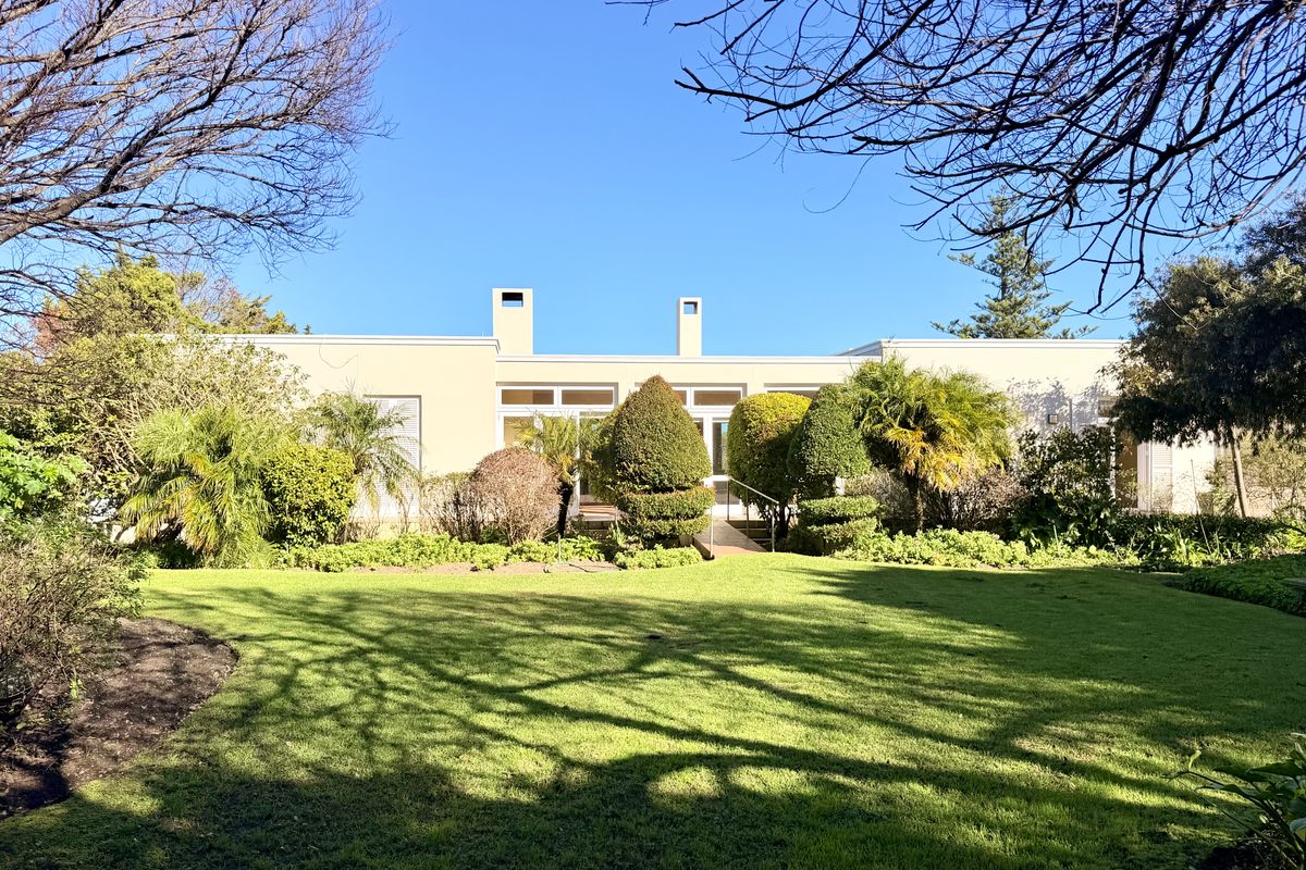 A well-maintained rear elevation of the house featuring large sliding glass doors, dual chimneys, and a spacious, manicured garden with mature landscaping.