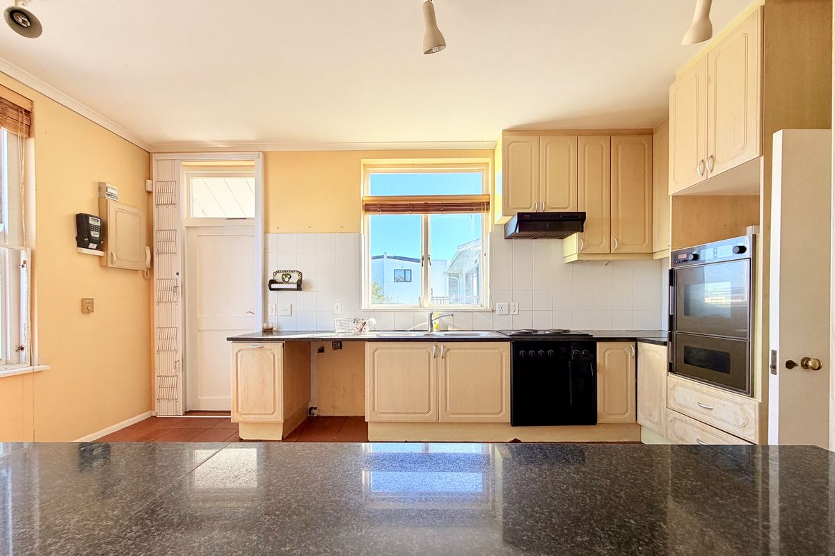 A functional kitchen featuring light-toned cabinetry, a built-in oven, electric hob, and a dark granite countertop with a tiled splashback.