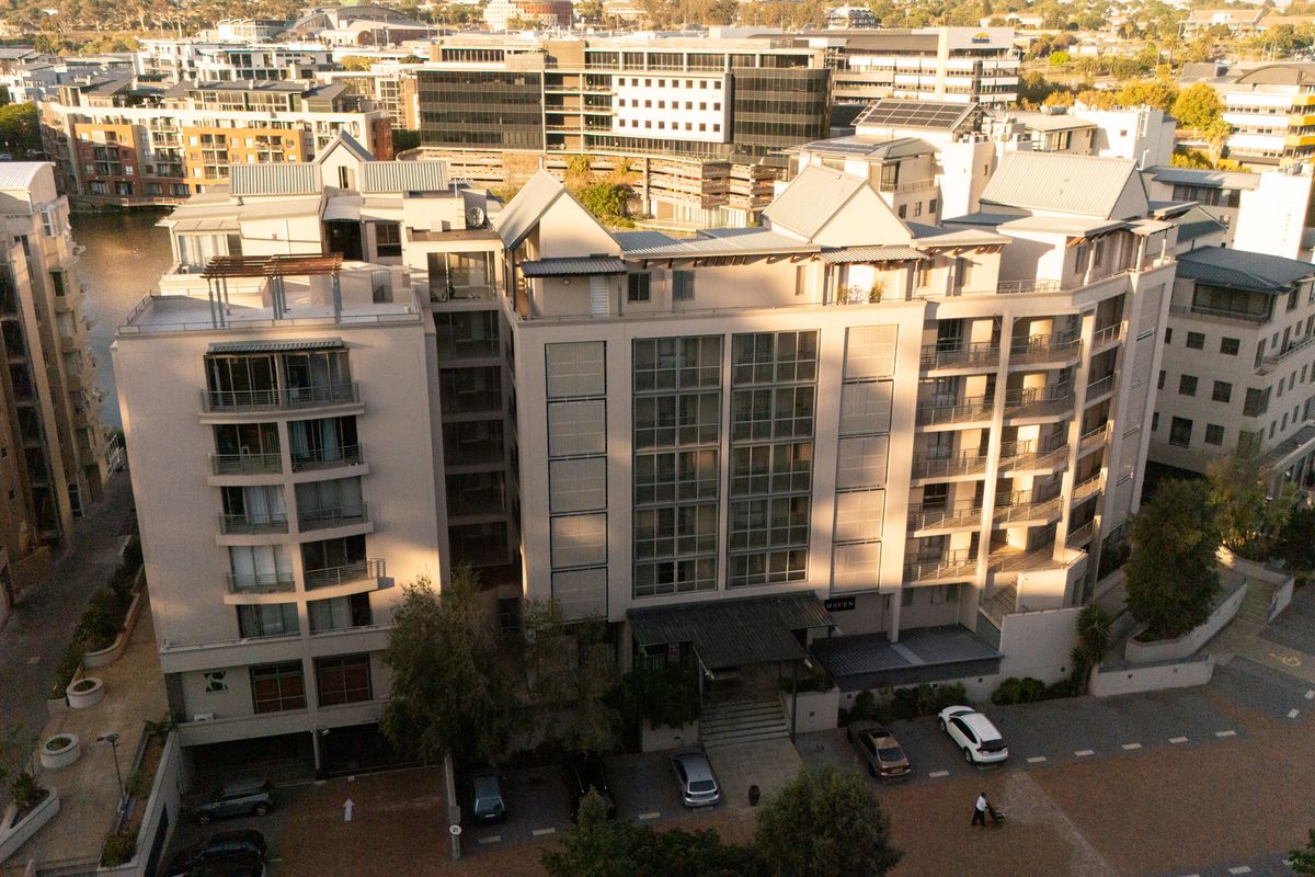 Aerial view of a multi-story apartment complex featuring modern architectural design, private balconies, and a paved ground-level entrance area.