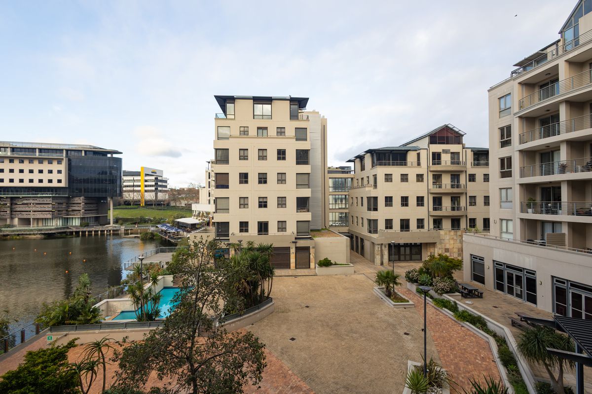 An elevated view of the apartment complex courtyard, featuring a swimming pool, paved communal areas, and direct waterfront access.
