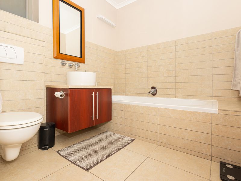 A modern bathroom featuring a wall-mounted toilet, a vessel sink with a vanity cabinet, and a tiled bathtub surround.