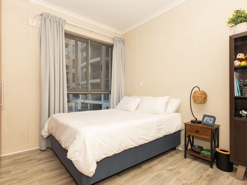 A well-maintained bedroom featuring laminate flooring, a built-in wardrobe, and a sliding window with neutral wall finishes.