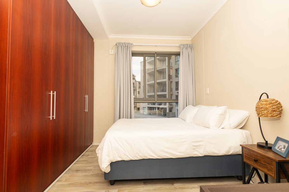 A well-maintained bedroom featuring floor-to-ceiling built-in cupboards, modern laminate flooring, and an aluminium-framed window providing natural light.