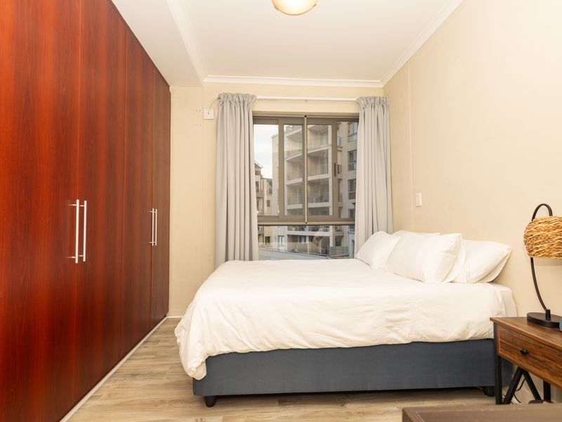 A well-maintained bedroom featuring floor-to-ceiling built-in cupboards, modern laminate flooring, and an aluminium-framed window providing natural light.