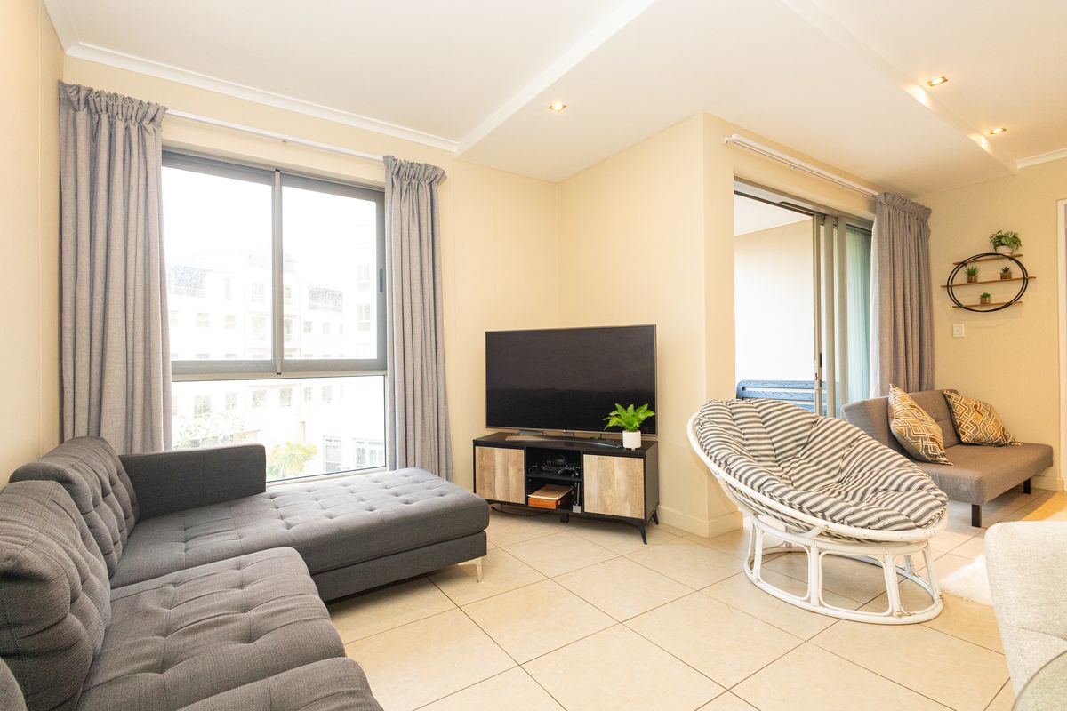 A bright and well-maintained living room featuring neutral tiled flooring, recessed lighting, and large sliding glass doors leading to an outdoor area.