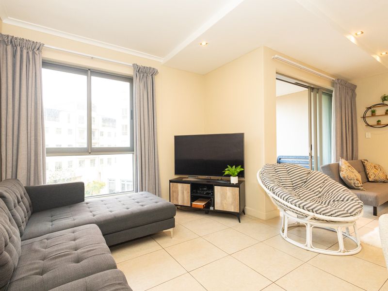 A bright and well-maintained living room featuring neutral tiled flooring, recessed lighting, and large sliding glass doors leading to an outdoor area.