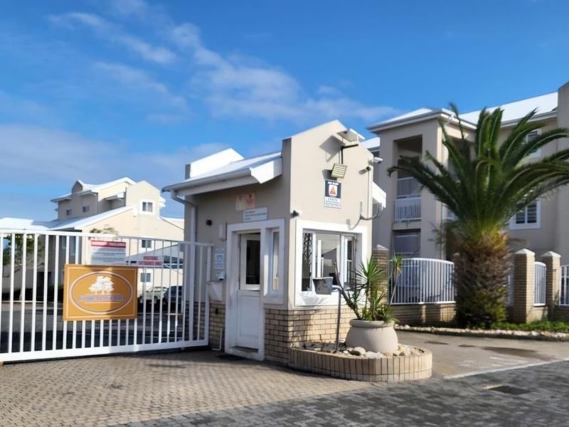 The entrance to the apartment complex features a secure gated access point with a dedicated guard house and paved driveway.