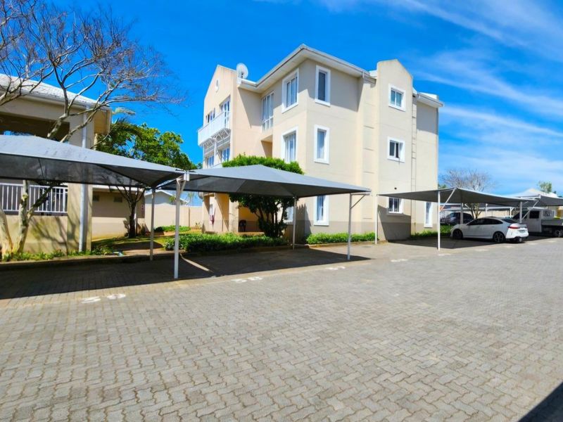 Exterior view of a multi-story apartment complex featuring paved parking areas with shade cloth carports and established landscaping.