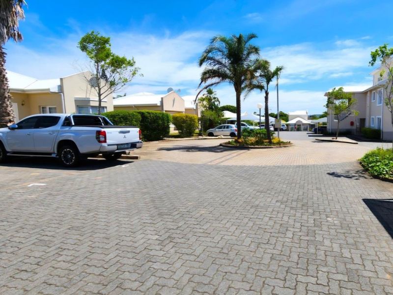 A well-maintained paved driveway and entrance area within a residential apartment complex, featuring landscaped garden beds and established palm trees.
