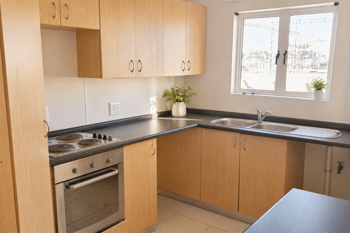 A functional kitchen featuring light wood cabinetry, dark laminate countertops, a built-in electric oven and hob, and a stainless steel double sink.
