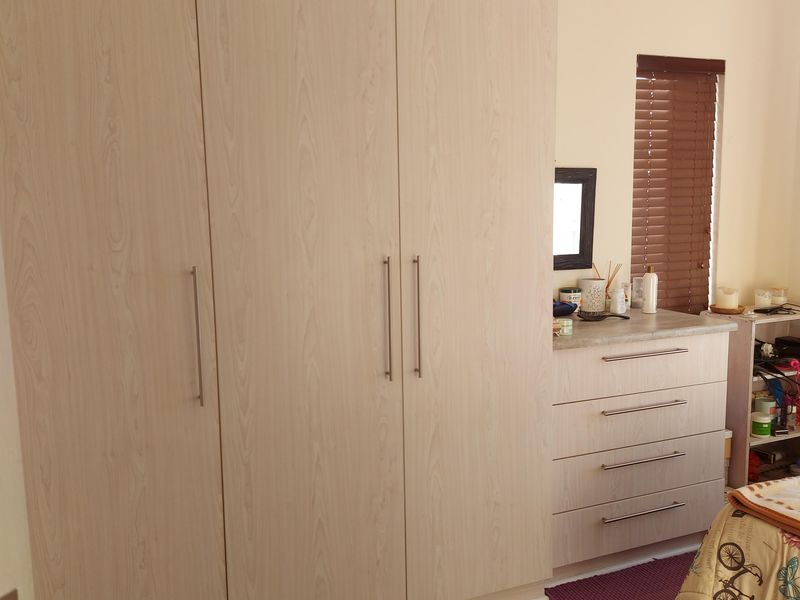 A well-maintained bedroom featuring light wood-grain built-in wardrobes, a matching built-in vanity unit, and modern laminate flooring.