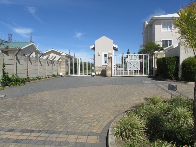 Secure gated entrance to the apartment complex featuring a guard house, paved driveway, and perimeter wall with electric fencing.