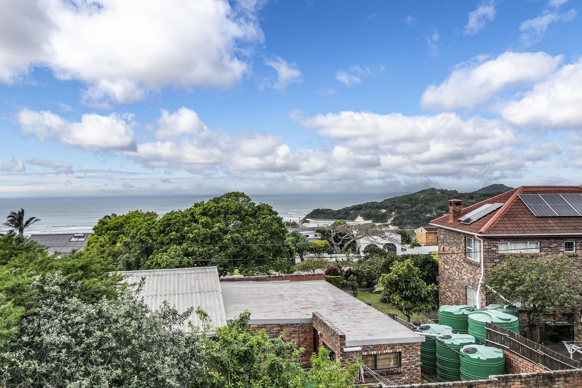 An elevated view overlooking a residential area with a coastal backdrop, featuring brick buildings, solar panels, and water storage tanks.