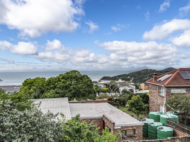 An elevated view overlooking a residential area with a coastal backdrop, featuring brick buildings, solar panels, and water storage tanks.