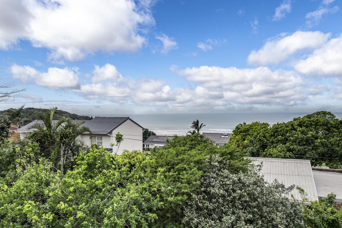 A scenic elevated view overlooking lush greenery, surrounding residential rooftops, and the distant coastline.