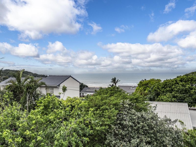 A scenic elevated view overlooking lush greenery, surrounding residential rooftops, and the distant coastline.