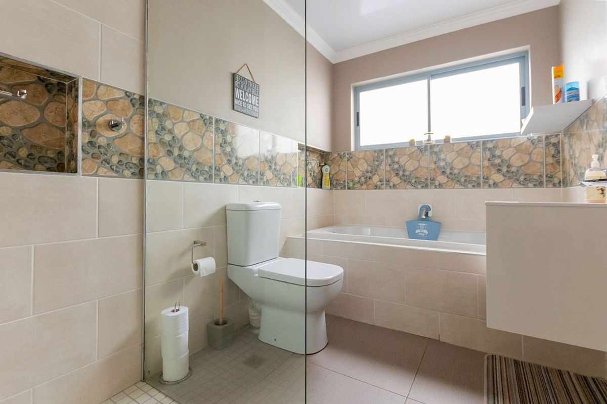A functional bathroom featuring a built-in bathtub, glass shower screen, and decorative tiled wall accents with a sliding window for natural light.