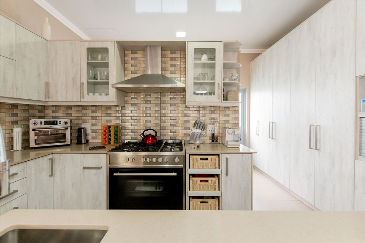 Modern kitchen featuring light wood-grain cabinetry, stone countertops, a gas hob with stainless steel extractor, and a decorative tiled backsplash.