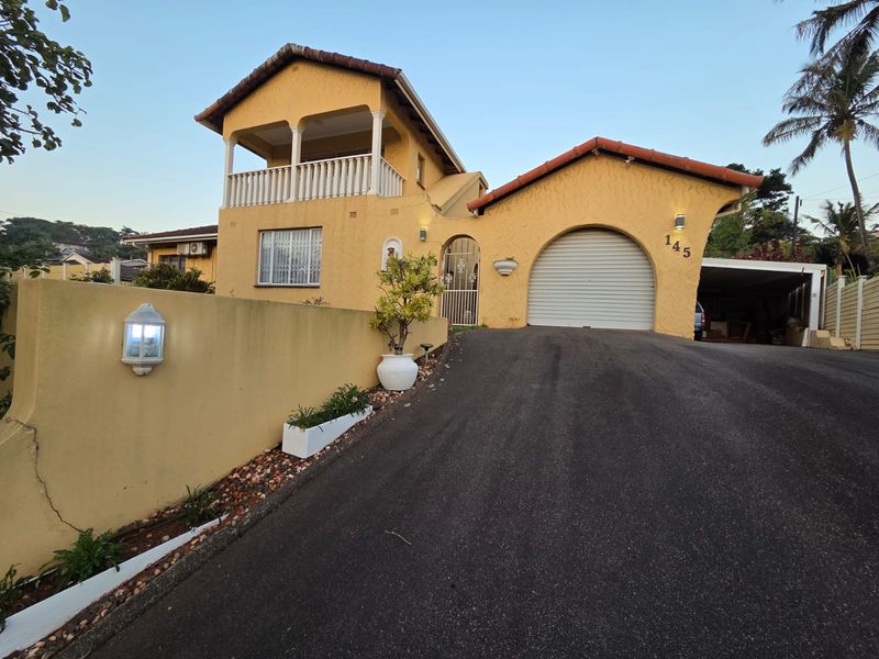 Front elevation of a two-story house featuring a balcony, arched garage entrance, and an asphalt driveway with a boundary wall.