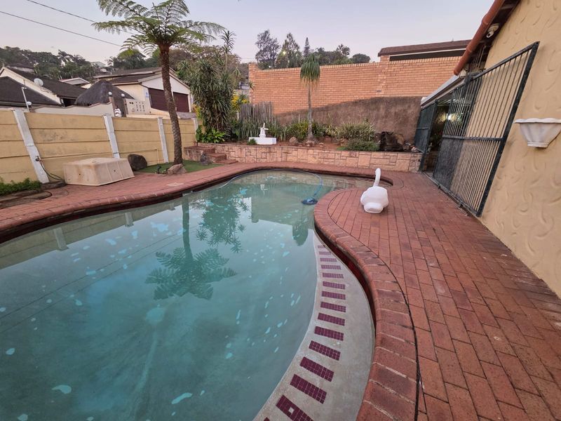 Outdoor pool area featuring a swimming pool with brick paving surround, enclosed by boundary walls and a security gate.
