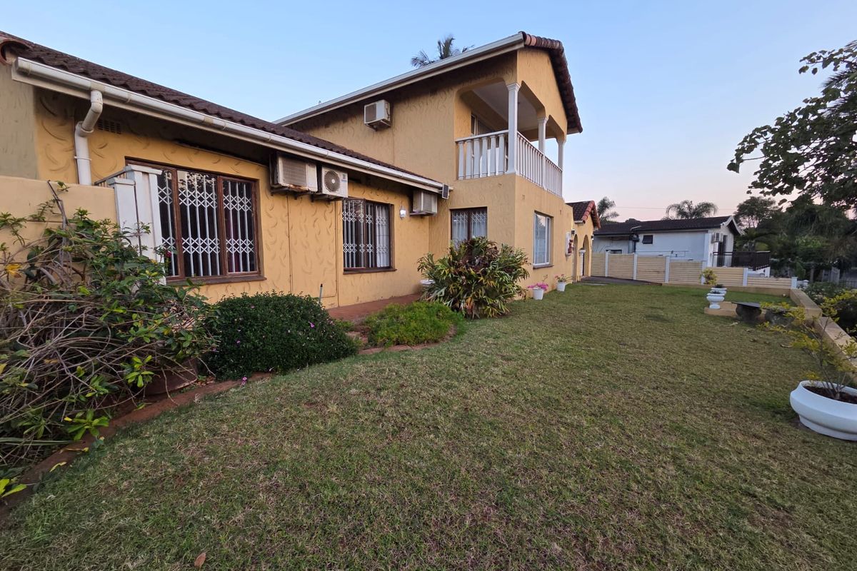 Rear view of a two-story house featuring a balcony, lawn, and exterior air conditioning units.