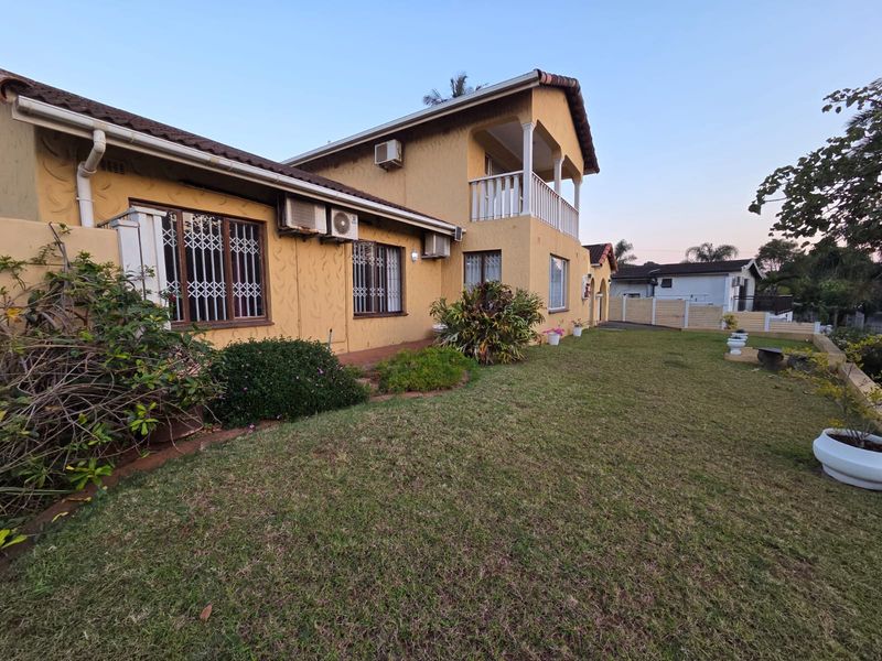Rear view of a two-story house featuring a balcony, lawn, and exterior air conditioning units.
