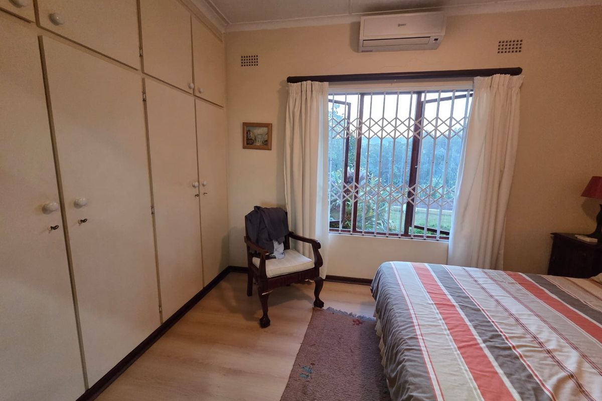 A bedroom featuring laminate flooring, extensive built-in cupboards, and a wall-mounted air conditioning unit, with a security gate fitted to the window.