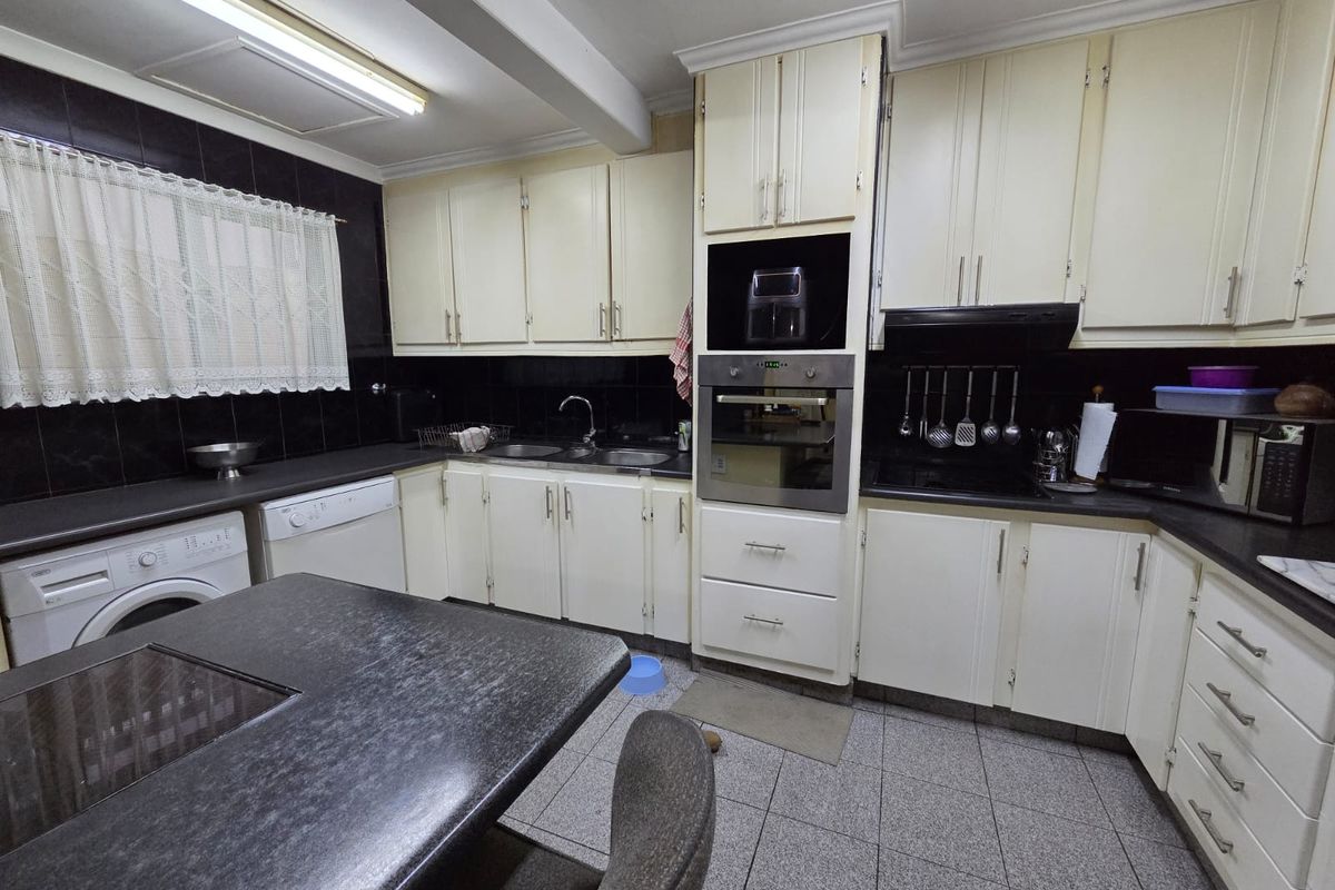 A functional kitchen featuring built-in cabinetry, integrated oven, double sink, and tiled finishes, offering a practical layout with potential for modern updates.